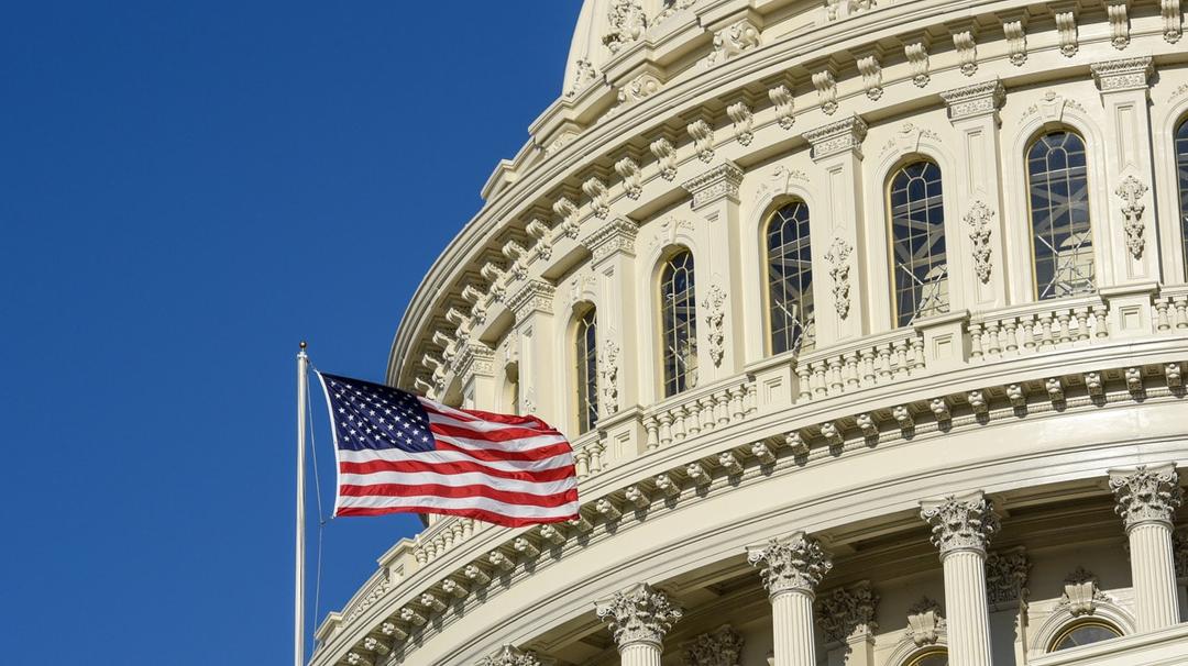 American flag waving in front of the ornate facade of the united states capitol building under a clear blue sky.