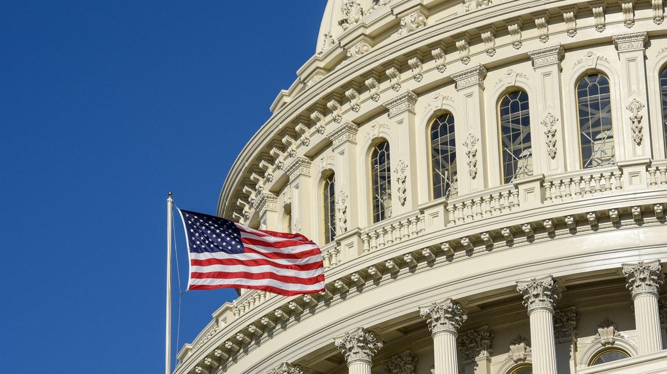 American flag waving in front of the ornate facade of the united states capitol building under a clear blue sky.