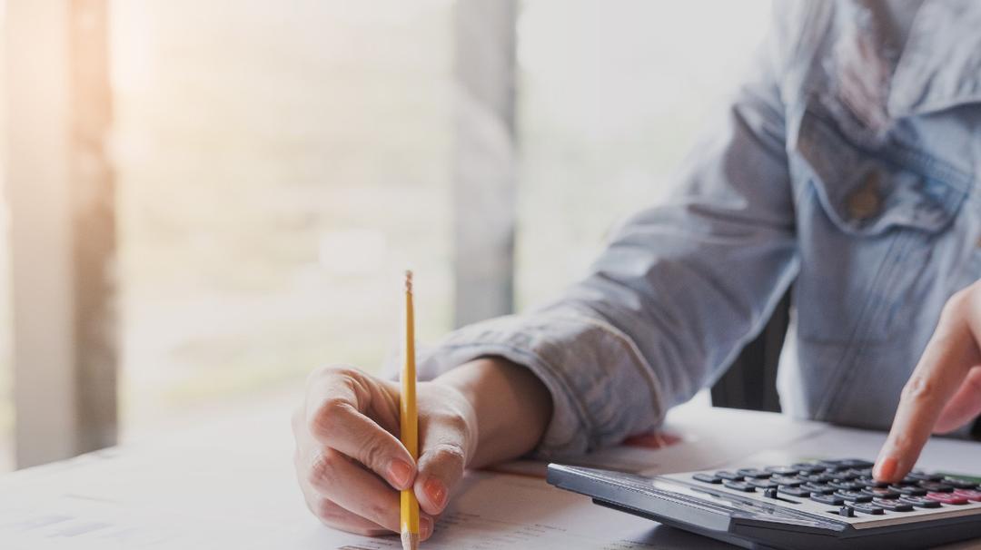 A person using a calculator and holding a pencil while reviewing documents at a desk.