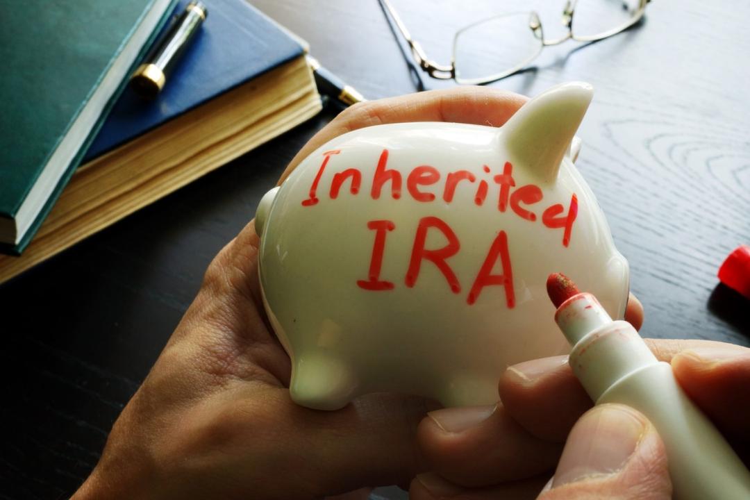 A person writing "inherited ira" on a piggy bank with a red marker, with glasses and books in the background.